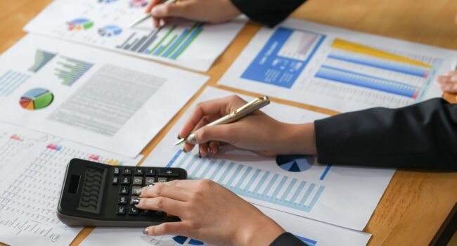 Accountants are analyzing data from the graph of the organization.They use the calculator and point the pen at the graphs.